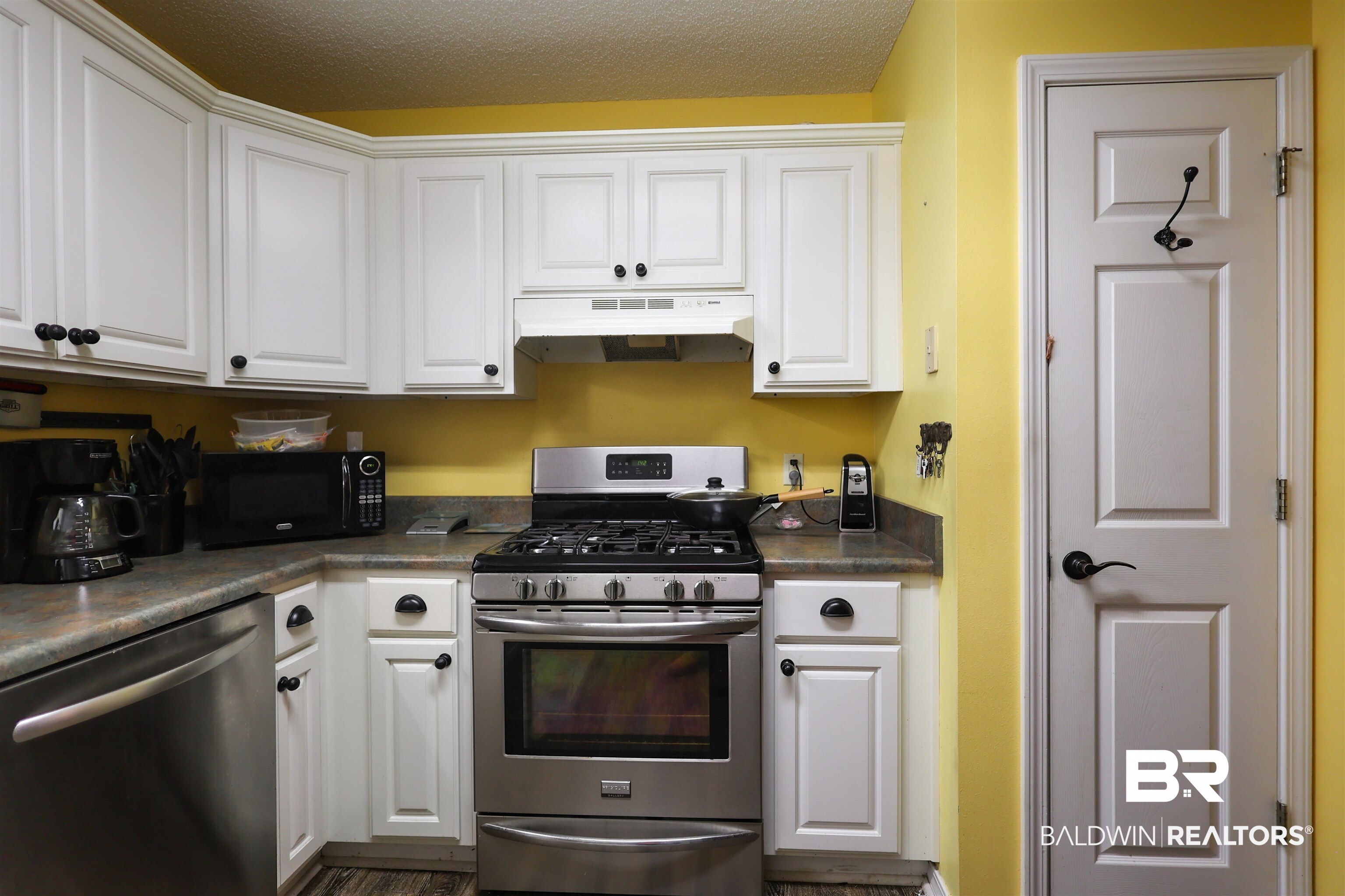 7790 Audubon Drive Foley, AL 36535 - Photo 9 of 39 Corner kitchen featuring white cabinetry with black hardware, stainless steel gas range, and a white range hood