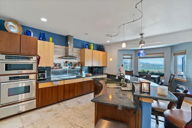 a kitchen with stainless steel appliances granite countertop a stove top oven a sink dishwasher a dining table and chairs with wooden floor