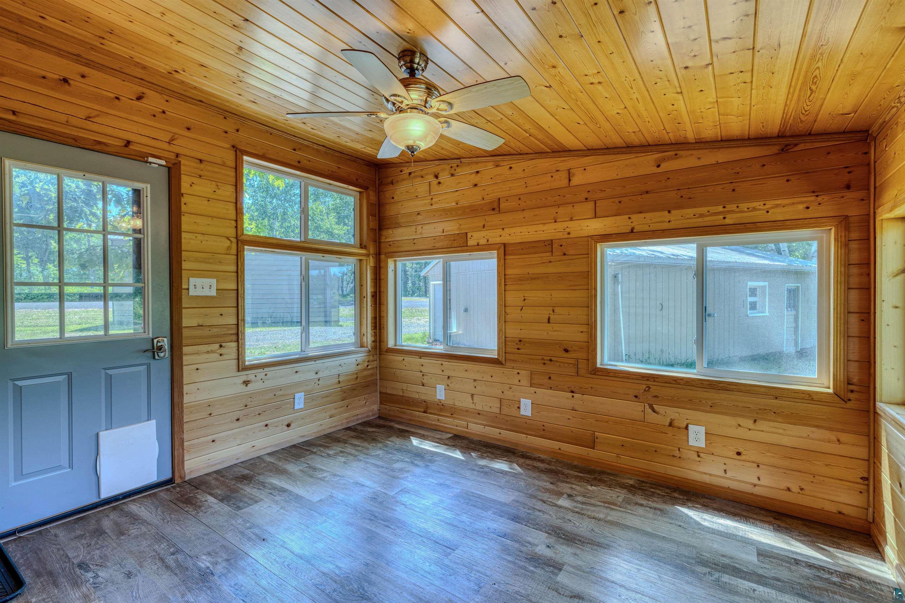66075 Rooster Road Iron River, WI 54847 - Photo 16 of 52 Wood-paneled room featuring multiple windows, a ceiling fan with integrated lighting, wood-finish flooring, and a paneled entry door with glass inserts