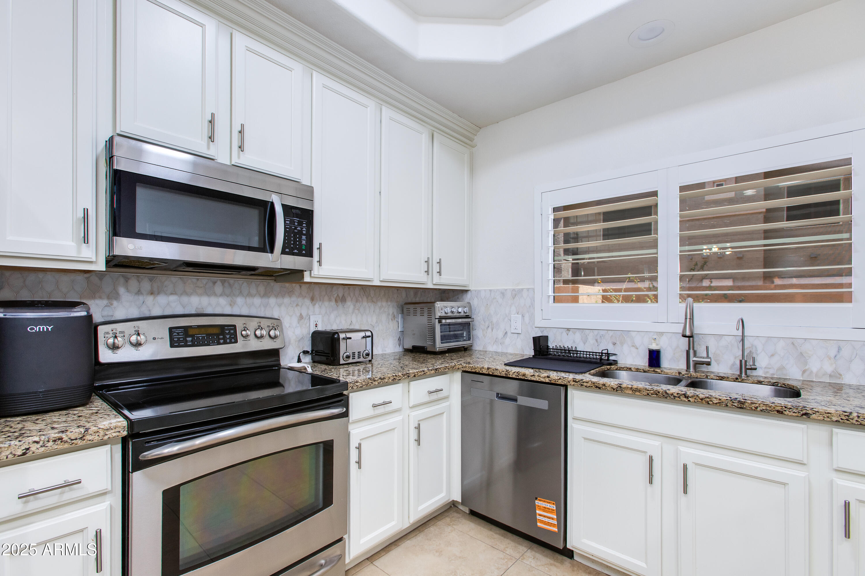 8245 East Bell Road, Unit 102 Scottsdale, AZ 85260 - Photo 9 of 21 a kitchen with granite countertop white cabinets appliances a sink and a window