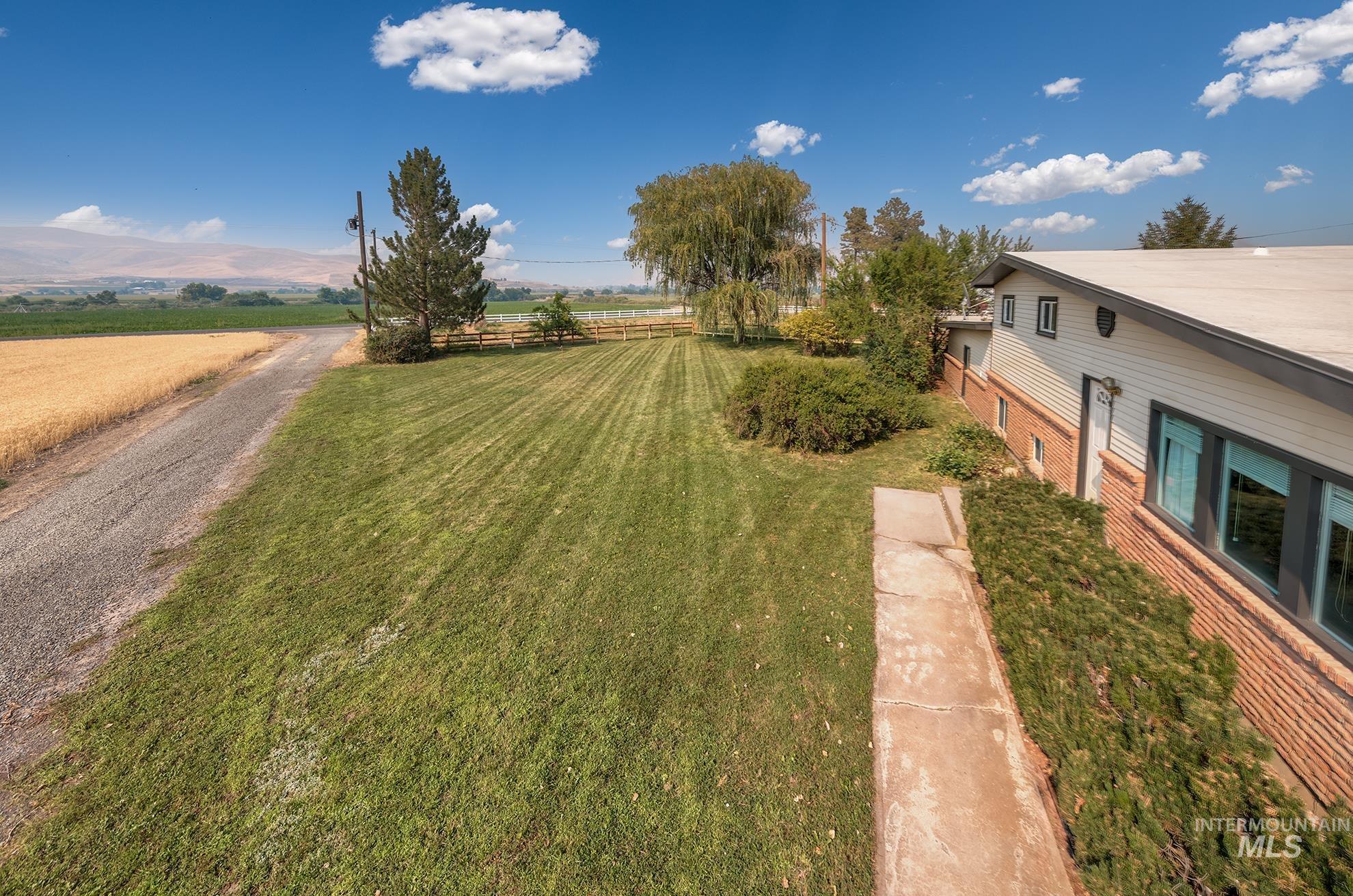 1741 Cove Road Weiser, ID 83672 - Photo 43 of 46 Expansive grounds featuring manicured lawn with professional striping, mature landscape plantings including weeping willow and evergreen trees, and a modern residential structure with brick and metal siding