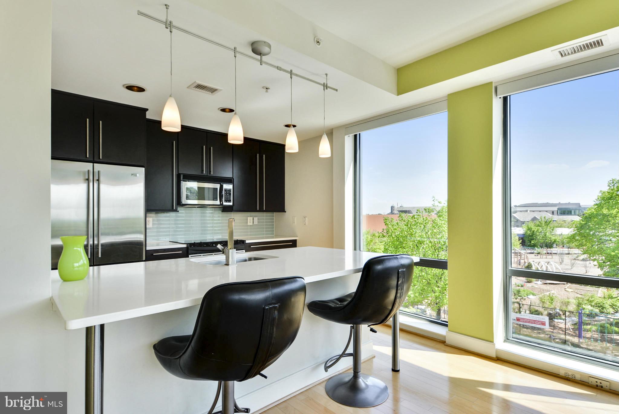 4101 Albemarle Street Northwest, Unit 337 Washington, DC 20016 - Photo 7 of 30 a kitchen with stainless steel appliances kitchen island granite countertop a table chairs in it and wooden floors