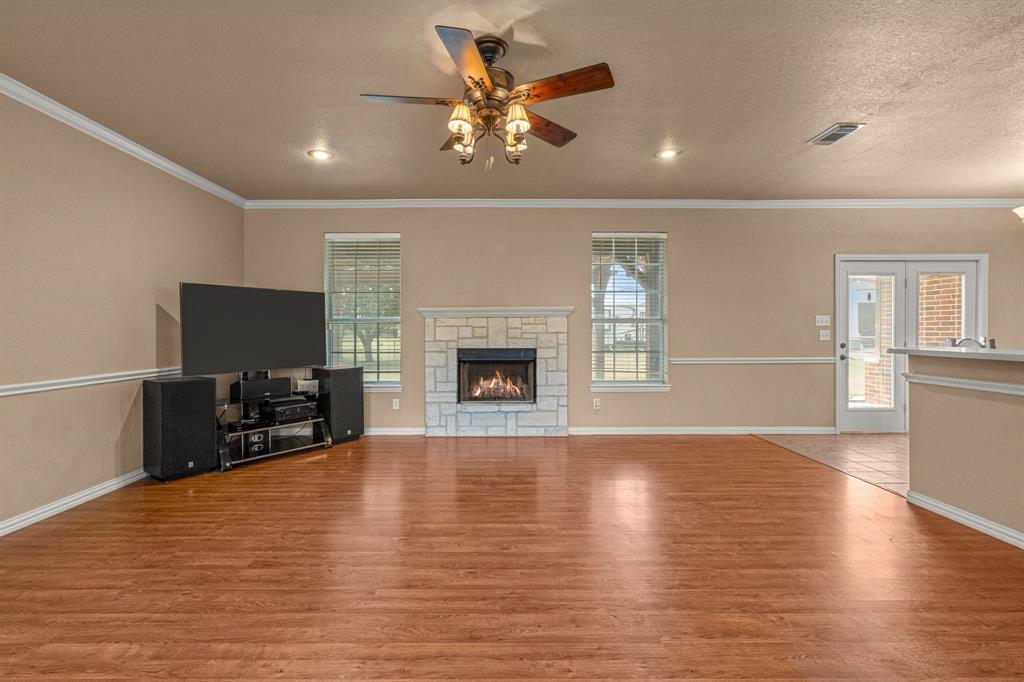 6501 Indian Trail Sanger, TX 76266 - Photo 6 of 39 Unfurnished living room featuring wood finished floors, ornamental molding, a stone fireplace, ceiling fan, and a textured ceiling