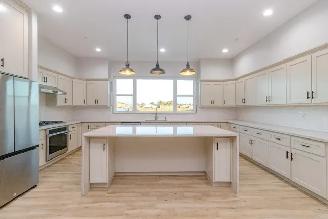 a kitchen with stainless steel appliances granite countertop a sink a stove a refrigerator and white cabinets with wooden floor