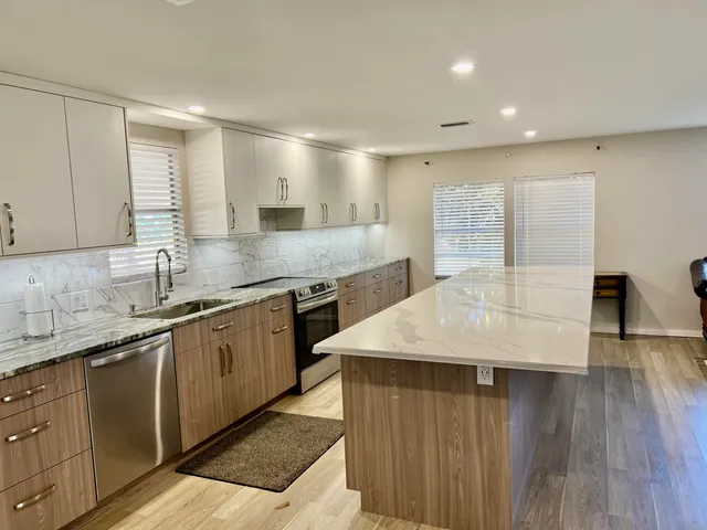 a living room with stainless steel appliances kitchen island a table chairs and a refrigerator