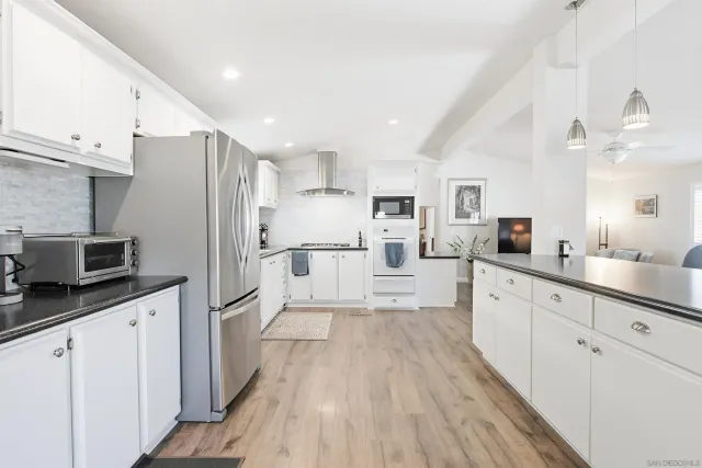 a large kitchen with stainless steel appliances kitchen island granite countertop a refrigerator a sink dishwasher a stove and white cabinets with wooden floor