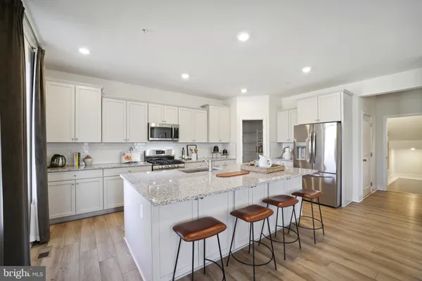 a kitchen with stainless steel appliances granite countertop a stove top oven a refrigerator a sink and white cabinets with wooden floor