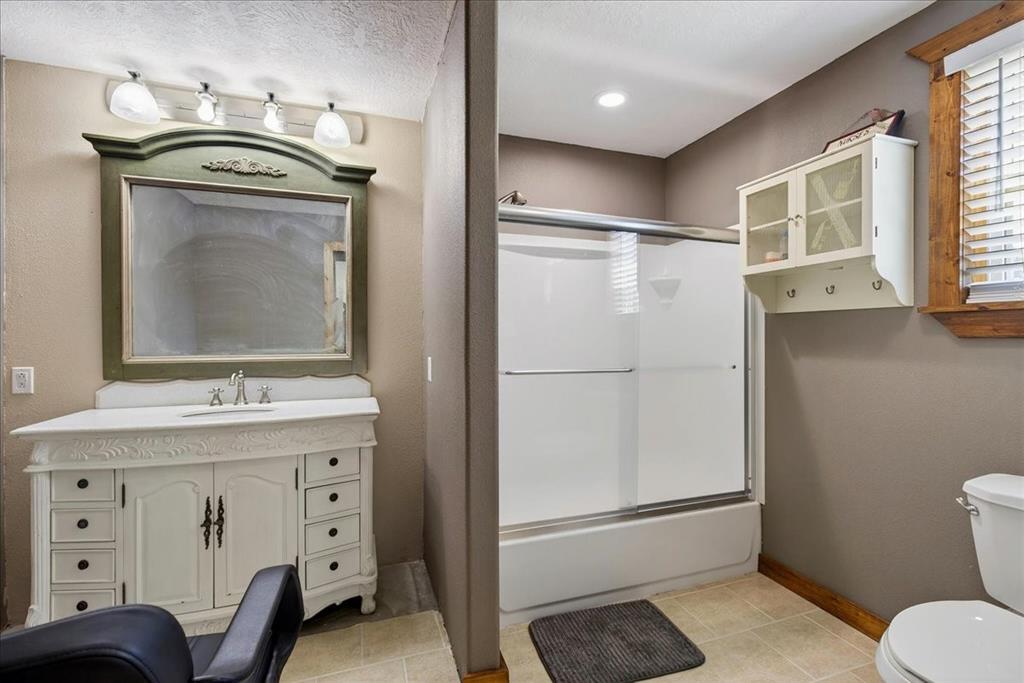 11591 Farm To Market 59 Athens, TX 75751 - Photo 27 of 40 4th Bathroom in Basement levelfeaturing a decorative vanity with an integrated sink, a large framed mirror, and a shower-tub combination with a sliding glass door. Next to this space is a Utility room.