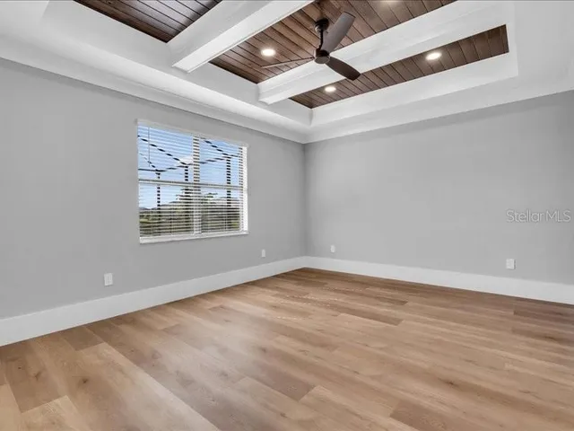 an empty room with wooden floor chandelier fan and windows