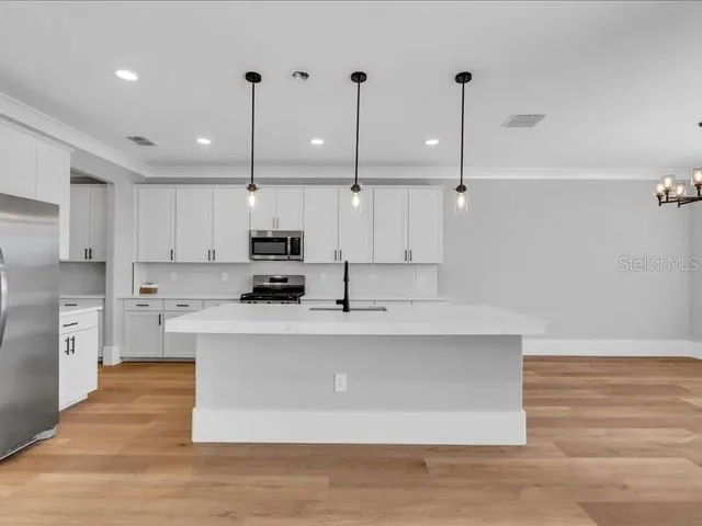 a large kitchen with stainless steel appliances granite countertop a sink a stove a refrigerator and white cabinets with wooden floor