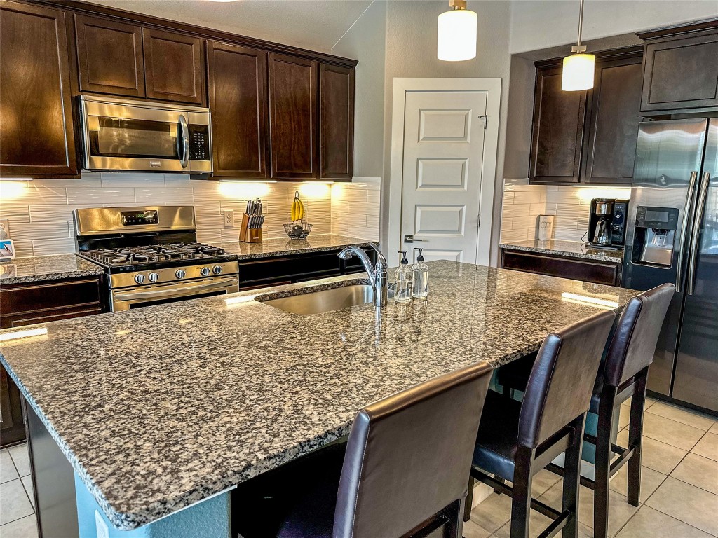 7216 Sienna Rouge Path Austin, TX 78744 - Photo 2 of 37 a kitchen with stainless steel appliances kitchen island granite countertop a stove top oven a sink a counter space and cabinets