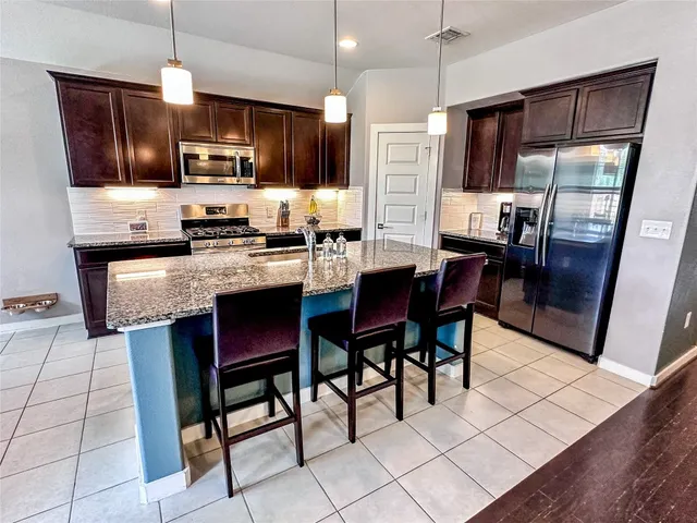 a kitchen with stainless steel appliances granite countertop a stove a refrigerator a sink dishwasher a dining table and chairs with wooden floor