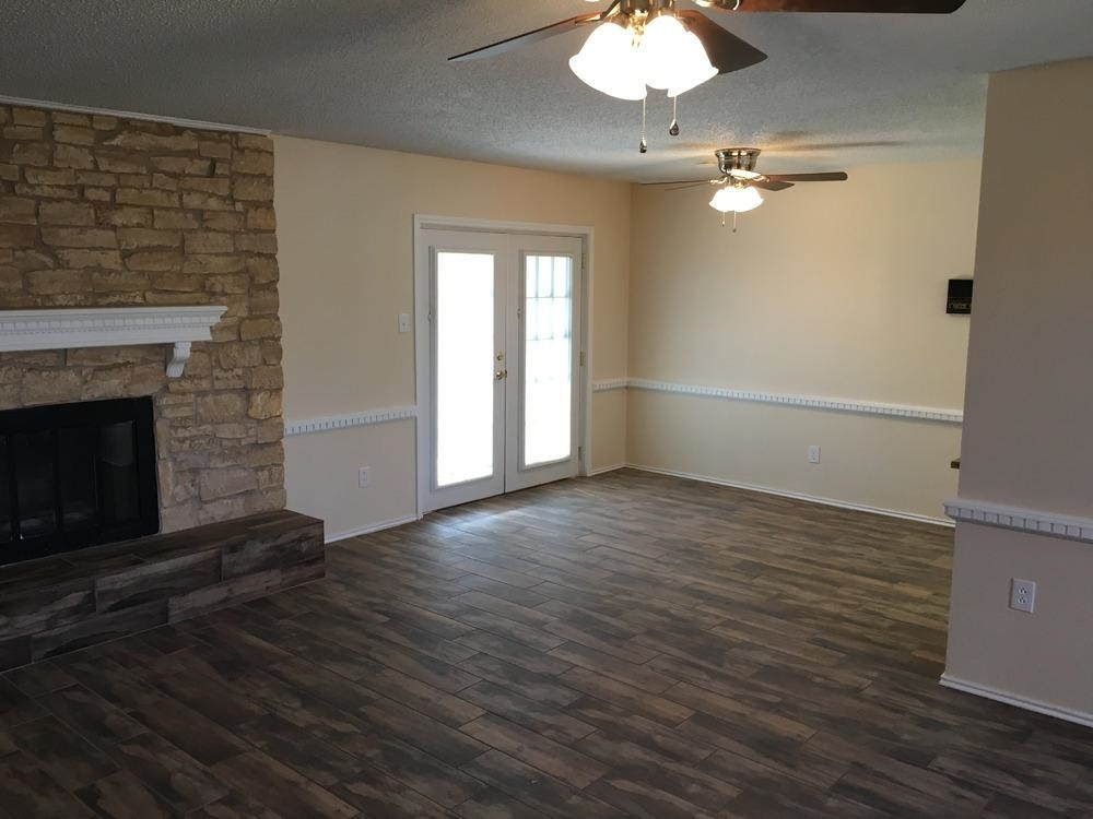 5739 Emory Street Lubbock, TX 79416 - Photo 4 of 10 an empty room with wooden floor fireplace and chandelier