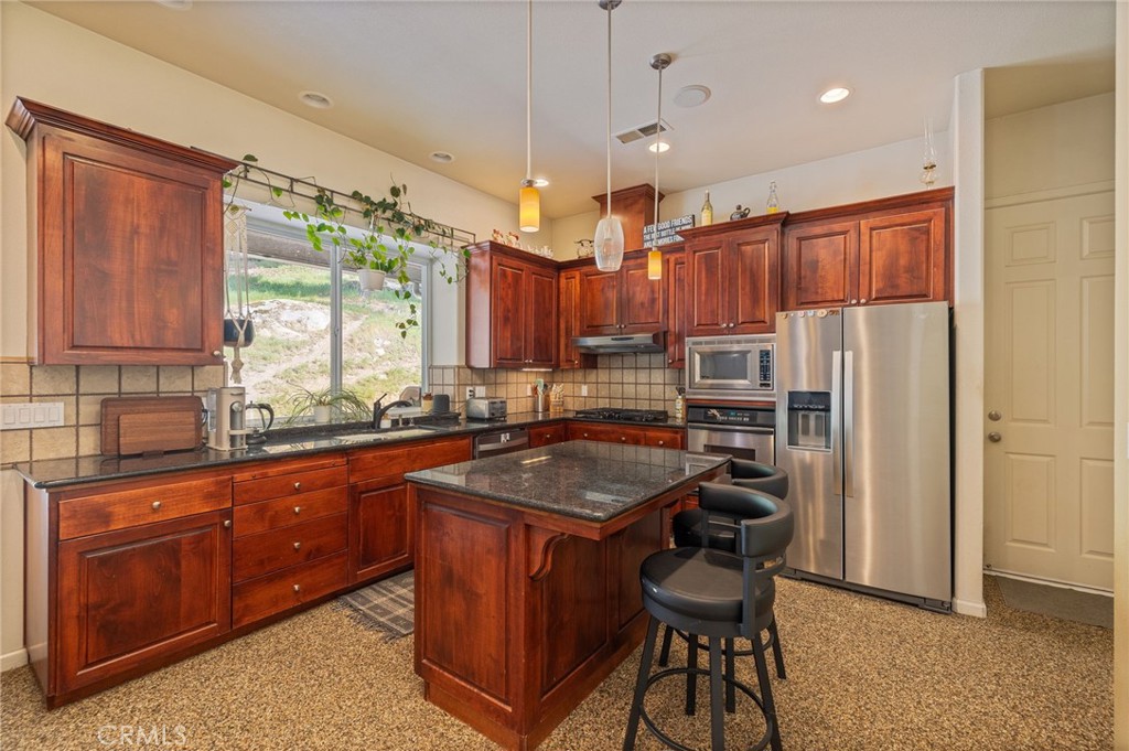 36919 Deer Path Circle Coarsegold, CA 93614 - Photo 15 of 59 a kitchen with kitchen island granite countertop wooden cabinets a sink a center island and stainless steel appliances