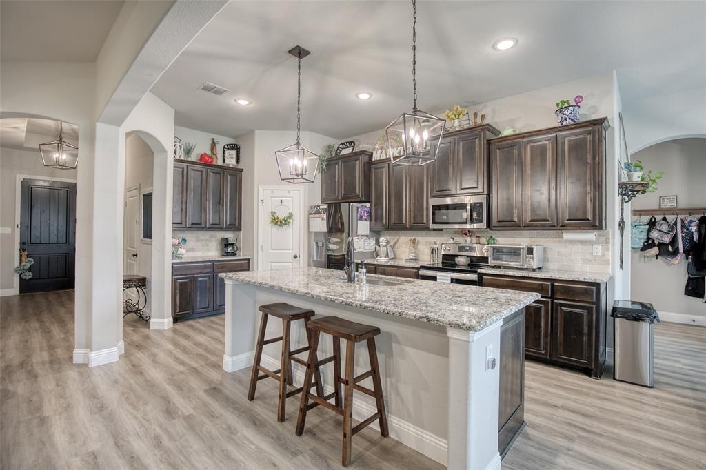 211 Rees Avenue Godley, TX 76044 - Photo 7 of 18 a kitchen with kitchen island granite countertop wooden floors and stainless steel appliances