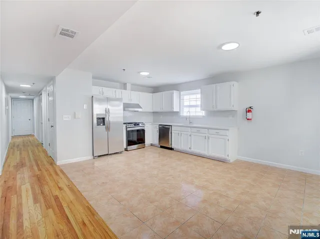 a large white kitchen with a stove a sink dishwasher and a refrigerator with wooden floor