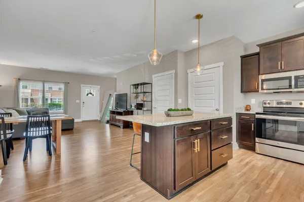 a kitchen with stainless steel appliances granite countertop a stove a sink dishwasher a refrigerator and a dining table with wooden floor