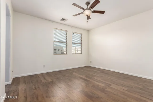 an empty room with wooden floor ceiling fan and windows