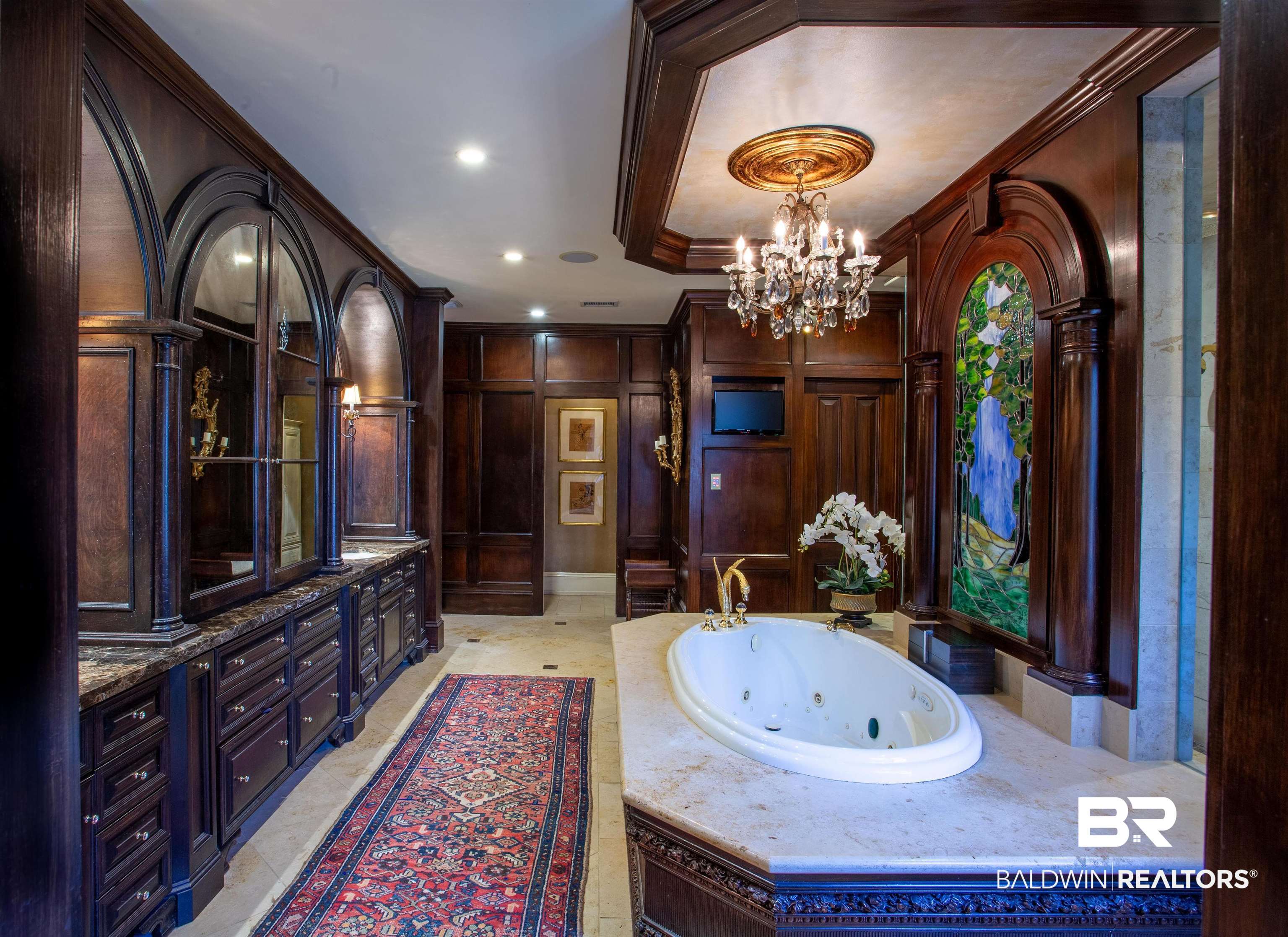 150 Austill Avenue Mobile, AL 36608 - Photo 27 of 39 Luxurious bathroom featuring a jetted soaking tub, dark wood paneling, ornate chandelier, built-in cabinetry with stone countertops, and a decorative stained-glass panel