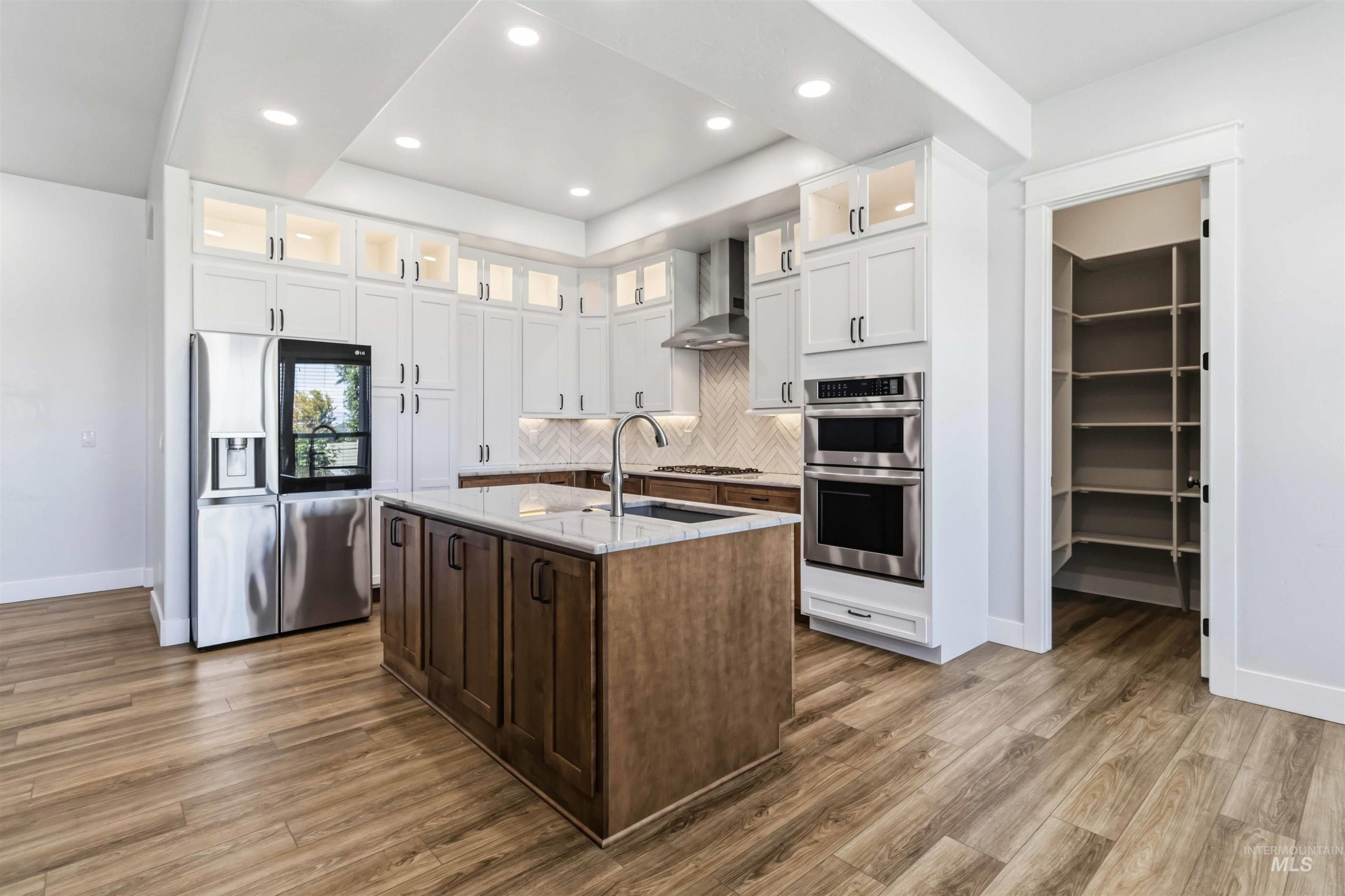 3218 North Cherry Laurel Way Star, ID 83669 - Photo 13 of 50 Modern kitchen featuring a central island with a sink, stainless steel appliances, herringbone tile backsplash, wood-finish flooring, and recessed lighting