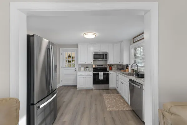 a kitchen with stainless steel appliances granite countertop a refrigerator oven a sink dishwasher and white cabinets with wooden floor