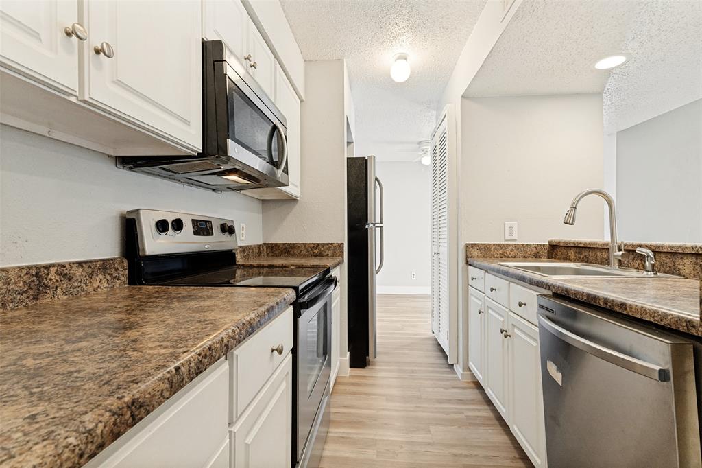 5522 Boca Raton Boulevard, Unit 404 Fort Worth, TX 76112 - Photo 3 of 12 Kitchen featuring white cabinetry, speckled countertops, stainless steel appliances, and wood-finish flooring