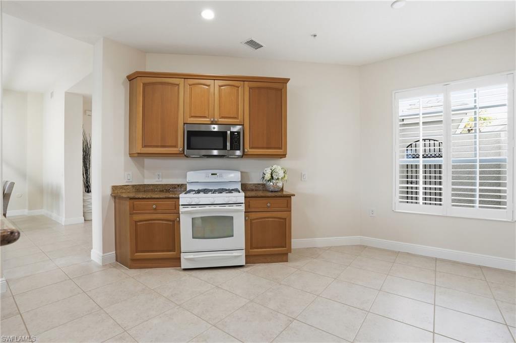 9263 Museo Circle, Unit 103 Naples, FL 34114 - Photo 9 of 49 Kitchen featuring gas range gas stove, stainless steel microwave, wood finish cabinets, dark stone counters, and light tile patterned floors