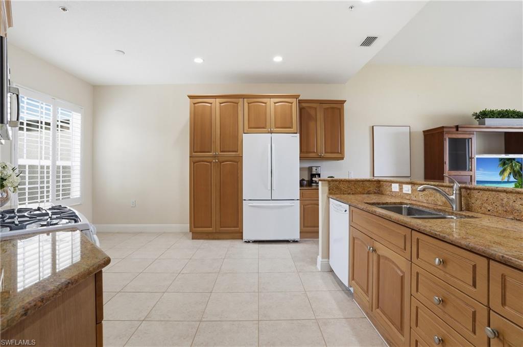 9263 Museo Circle, Unit 103 Naples, FL 34114 - Photo 10 of 49 Kitchen featuring light stone counters, white appliances, wood finish cabinetry, light tile patterned floors, and recessed lighting