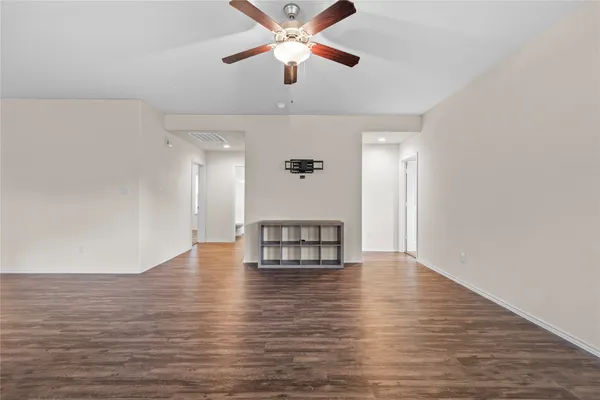 a view of an empty room with wooden floor and a ceiling fan