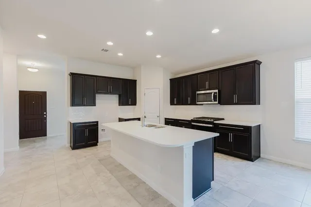 a kitchen with stainless steel appliances a stove top oven a sink a refrigerator and white cabinets