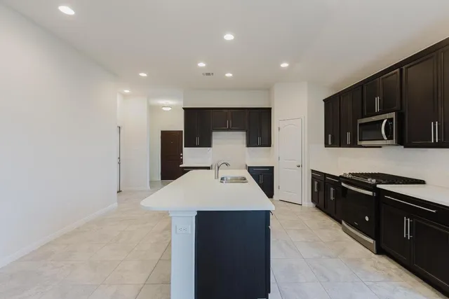 a large kitchen with stainless steel appliances a large counter top a stove a refrigerator a sink and a microwave oven