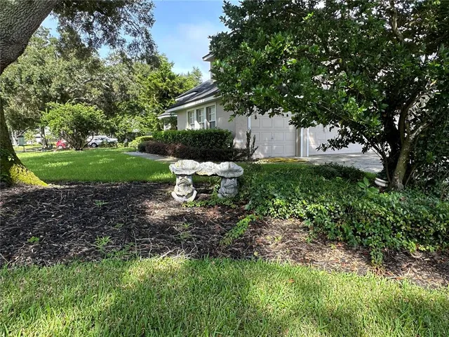 a white bench sitting in a yard with plants and large trees