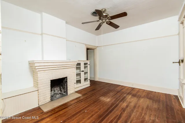 a view of a livingroom with a fireplace a ceiling fan and wooden floor