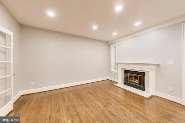 a view of an empty room with wooden floor fireplace and a window