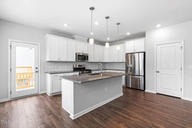 a kitchen with stainless steel appliances a refrigerator a sink dishwasher a stove and white cabinets with wooden floor