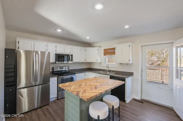 a kitchen with stainless steel appliances granite countertop a refrigerator a stove a sink dishwasher and white cabinets with wooden floor