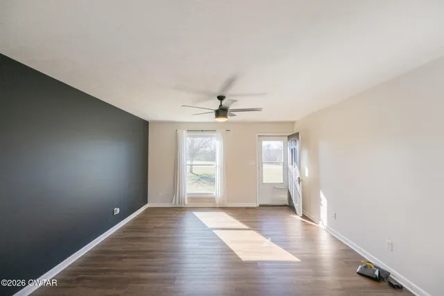 an empty room with wooden floor chandelier fan and windows