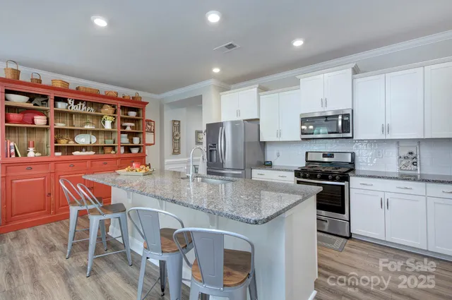 a kitchen with stainless steel appliances granite countertop a stove top oven a refrigerator a sink and chairs