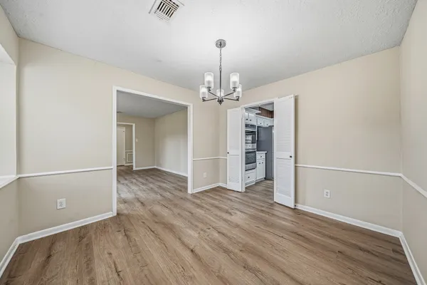 an empty room with wooden floor chandelier and windows