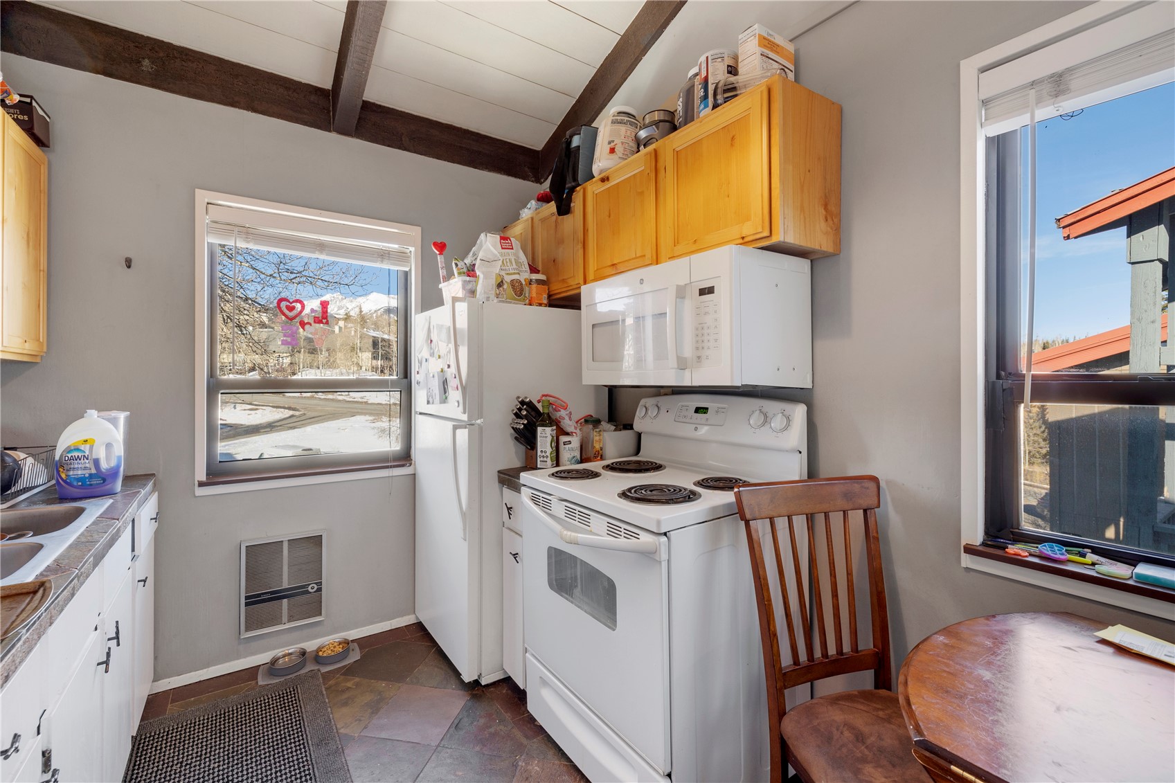 809 Ryan Gulch Road, Unit 809 Silverthorne, CO 80498 - Photo 12 of 17 Kitchen with white appliances, heating unit, light wood finish cabinetry, beamed ceiling, and light countertops