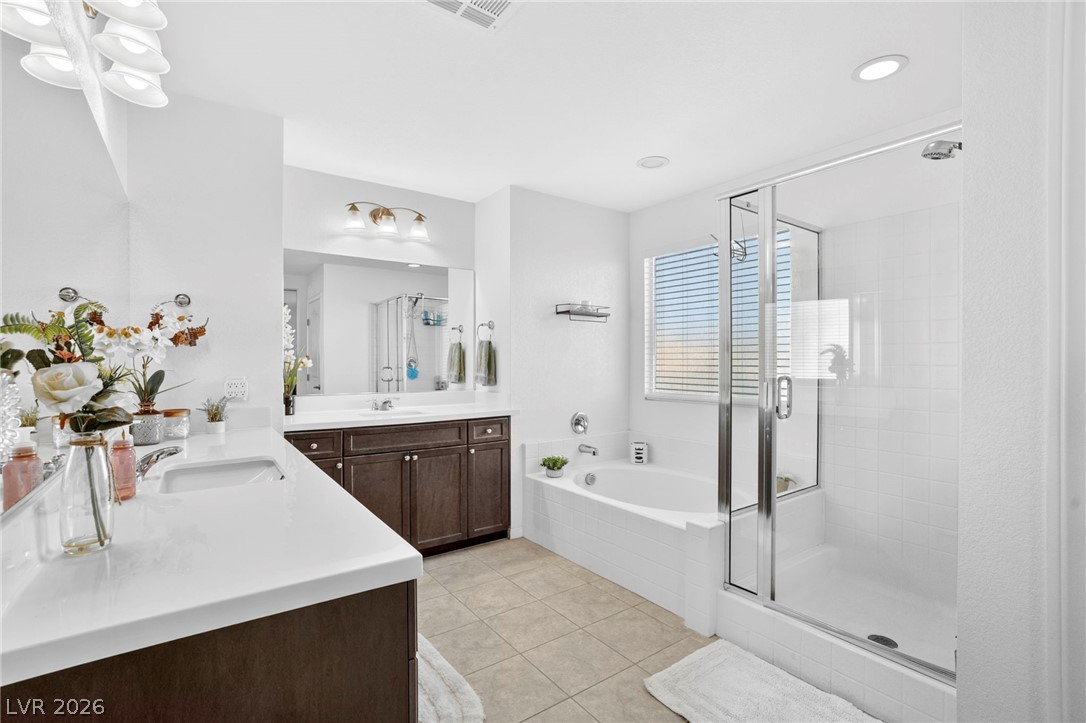 6281 Angora Peak Lane Las Vegas, NV 89115 - Photo 19 of 34 A well-appointed primary bathroom features a double vanity, a deep soaking tub, and a separate glass-enclosed shower.