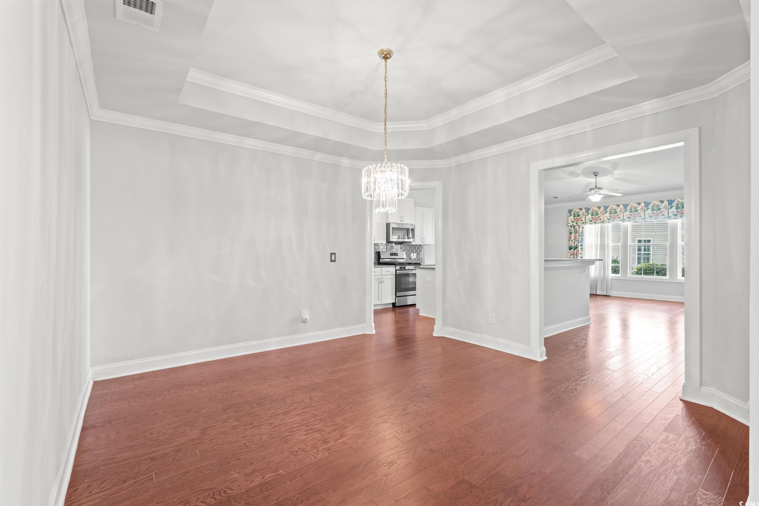 135 Parmelee Drive, Unit C Murrells Inlet, SC 29576 - Photo 8 of 37 Unfurnished dining area featuring a raised ceiling, a ceiling fan, dark wood-style flooring, crown molding, and a chandelier