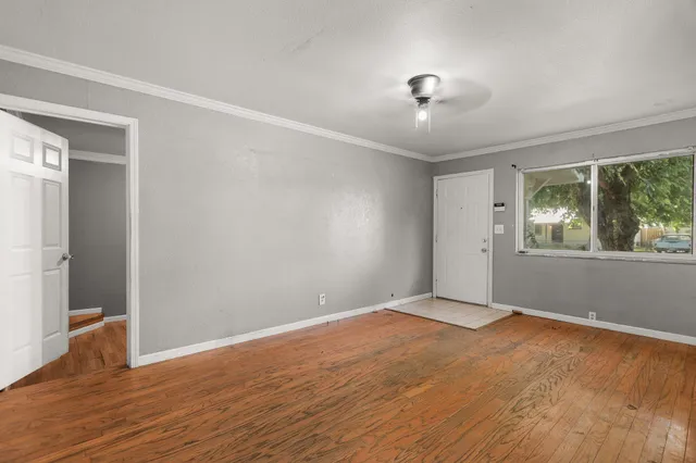 a view of an empty room with wooden floor and a window