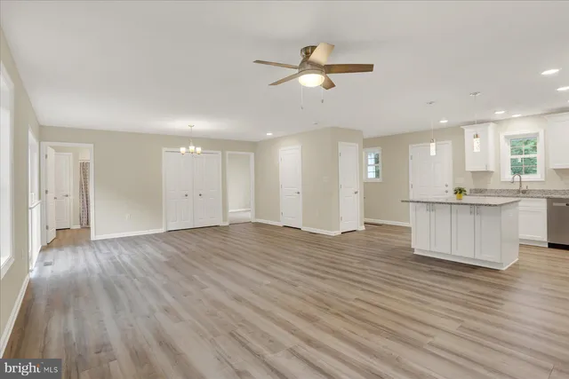 a view of an empty room and kitchen with wooden floor