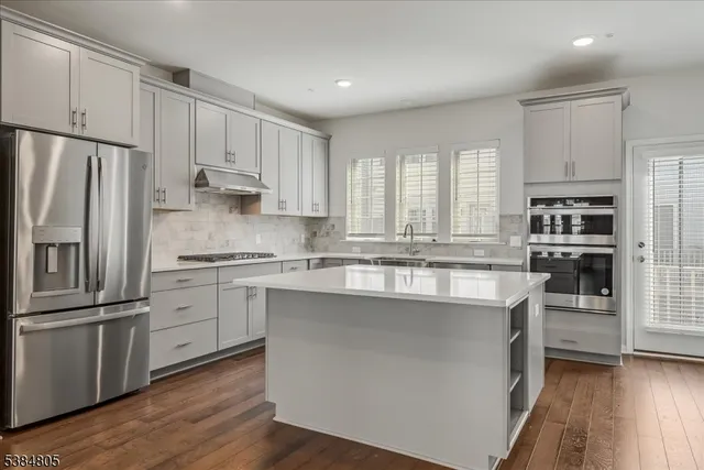 a kitchen with stainless steel appliances granite countertop a refrigerator a stove a sink and white cabinets with wooden floor