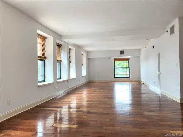 a view of an empty room with window and wooden floor