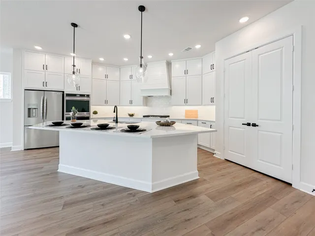 a kitchen view with stainless steel appliances kitchen island granite countertop a stove a refrigerator a oven and white cabinets with wooden floor