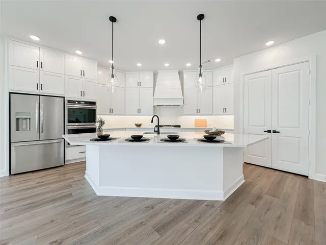 a large kitchen with stainless steel appliances a large counter top a refrigerator a fireplace and a wooden floor