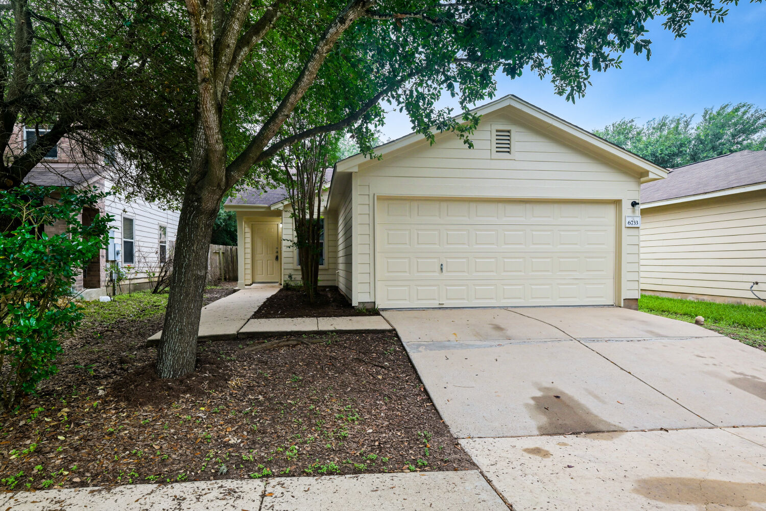 6733 Doyal Drive Austin, TX 78747 - Photo 2 of 28 A welcoming facade with mature trees and an attached garage offers appealing curb appeal.