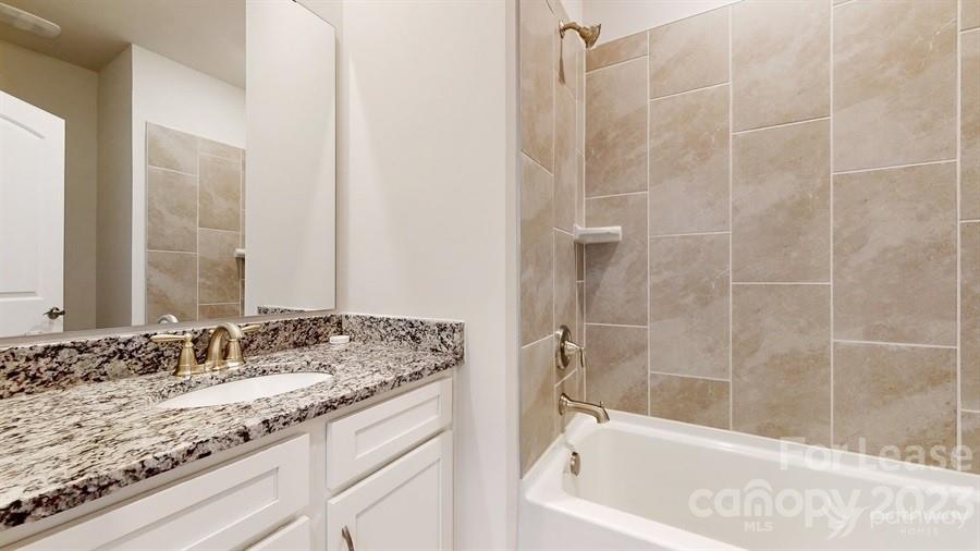 163 Tanner Loop Troutman, NC 28166 - Photo 16 of 27 a bathroom with a granite countertop sink a mirror and a bathtub
